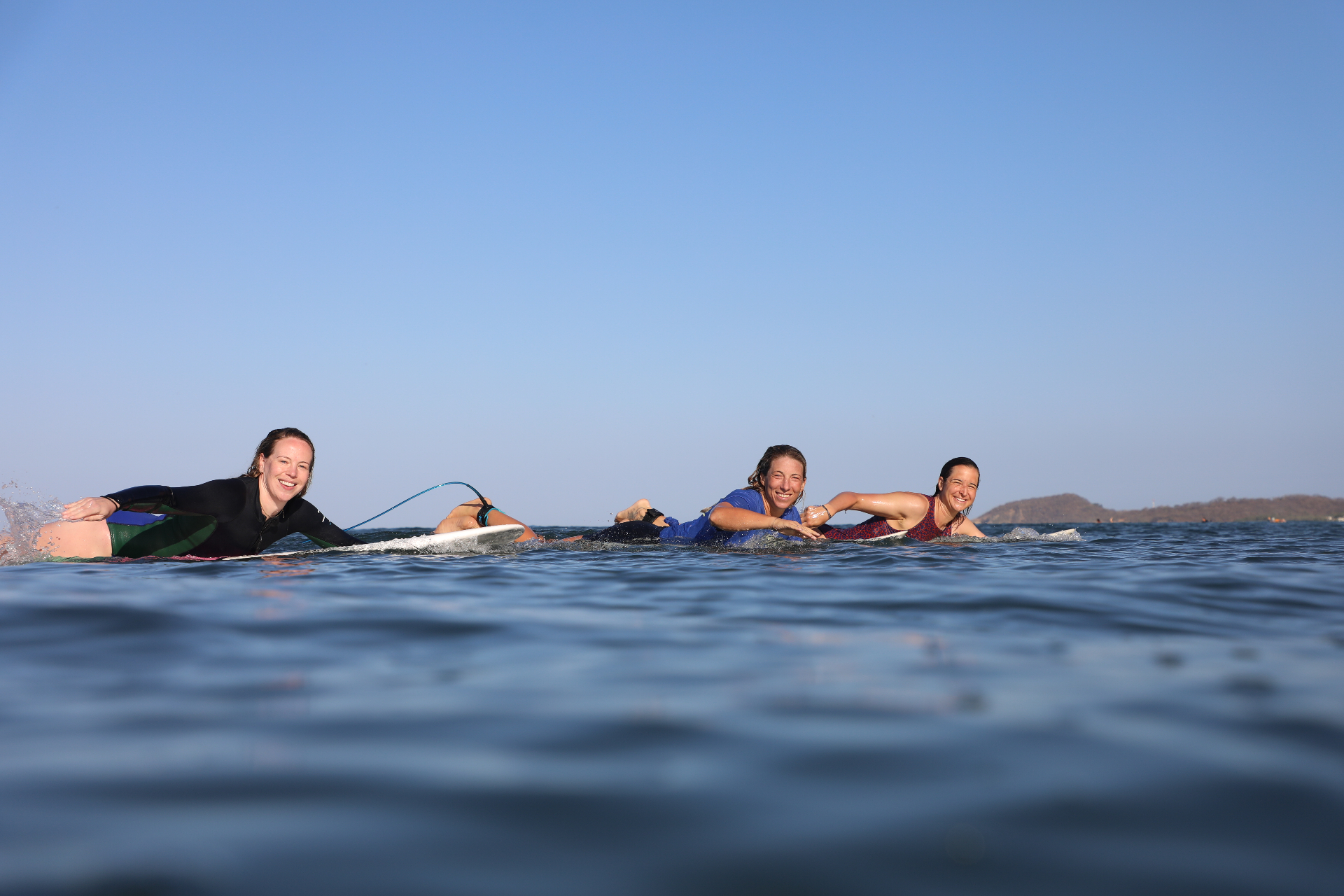 Three women smiling in the ocean on surfboards