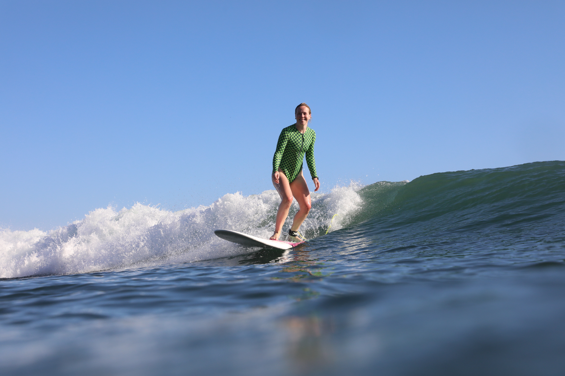 Woman smiling while surfing a wave in a green checkered wetsuit