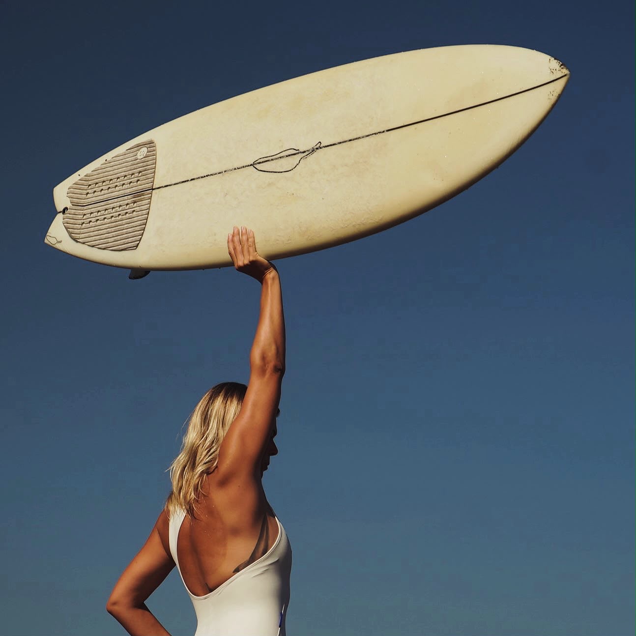 Katharine Derrey holding a surfboard against a clear blue sky